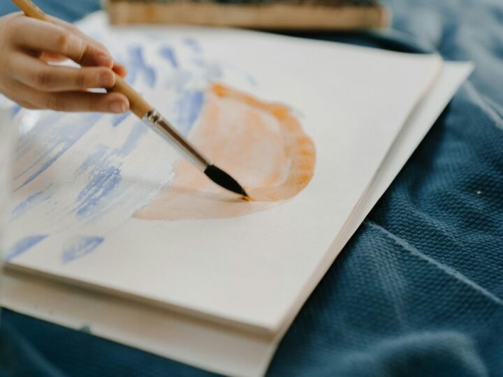A hand painting with a brush on paper during an art therapy session